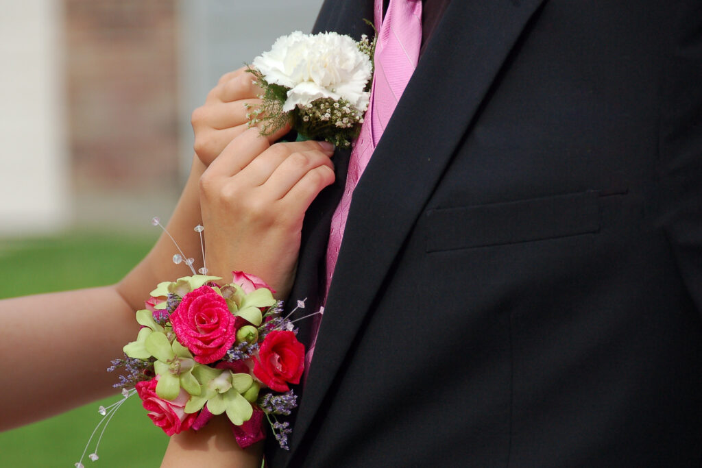 Young woman pins lapel corsage onto prom date